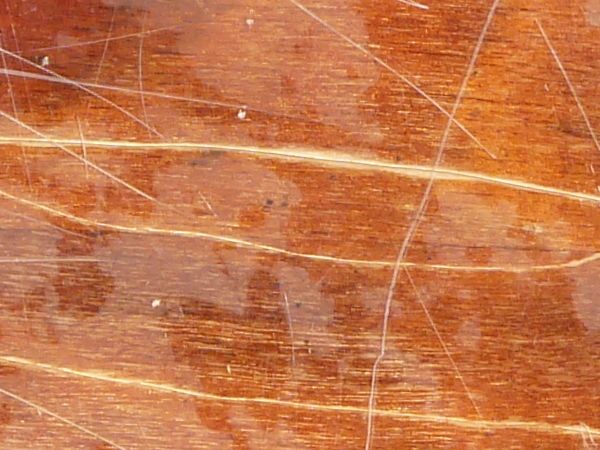Laquered wood texture, with a scratched, glossy surface covering the reddish brown board.